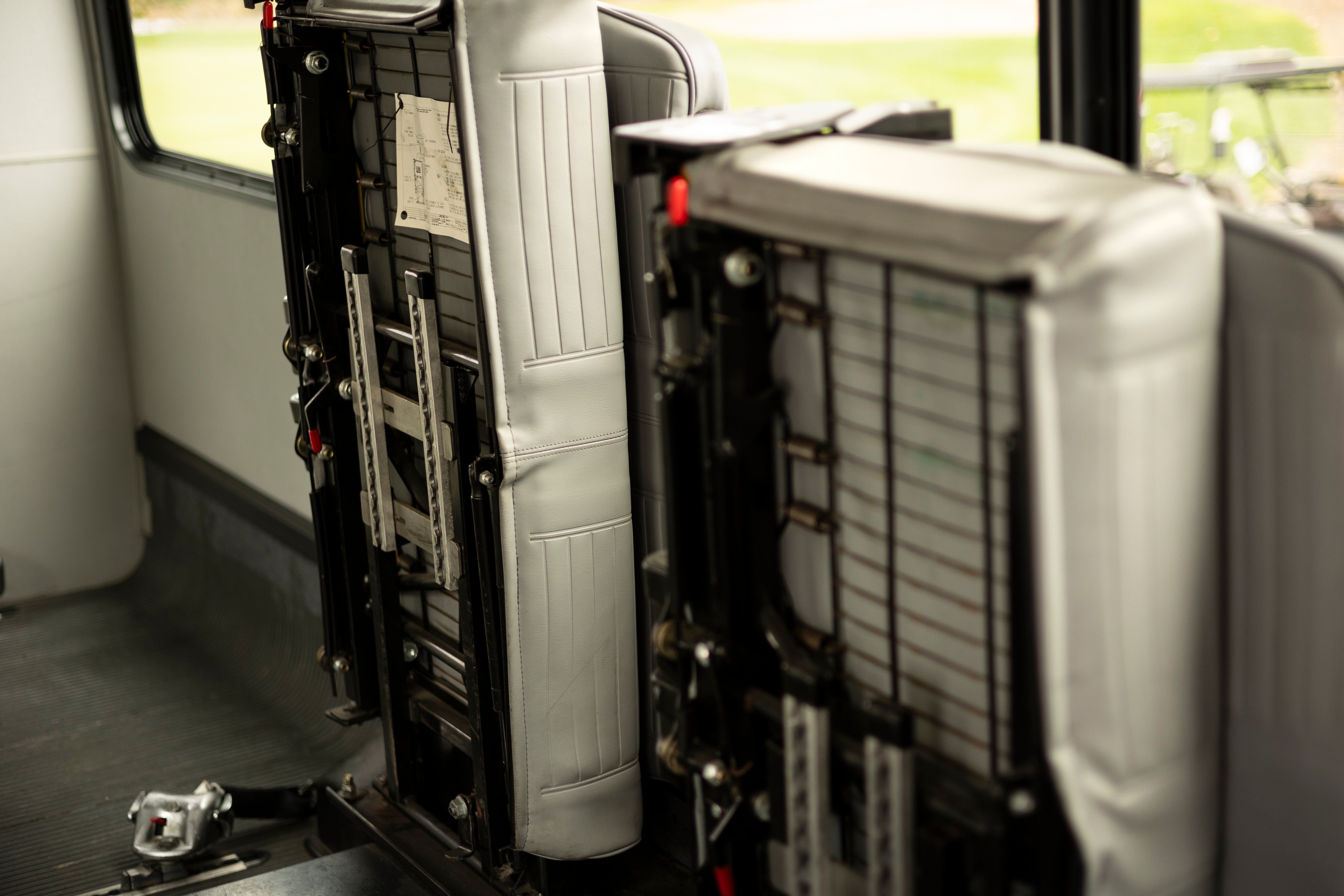 Two vehicle bench seats are pictured lifted vertically and secured into place, making more space in the back of a Ford E-350 cutaway with mobility van upfits.